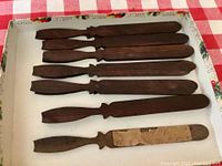 Twelve dark-stained wooden pieces resting in a box with one piece having an attached note.