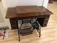 Front view of antique Singer sewing machine table with lift-top and side drawers, showing Singer treadle base and pedal.