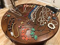 Wide view of all jewelry items laid out on wooden oval table showing necklaces, bracelets, pins, and earrings.
