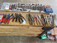 Overview of all tools including pliers, wrenches, drill bits, chains, and small hardware laid out on a wooden surface