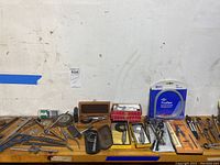 Top view of entire lot on wooden table showing diverse engineering and measuring tools including micrometers, compasses, calipers, and a TruFlex flexible measuring curve still in package.