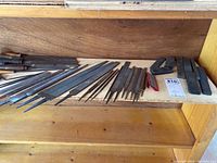 Shelf with multiple metal files arranged by size and shape along with rectangular sharpening stones and sharpening guide.