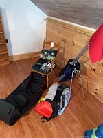 Wide shot of golf supplies showing a black golf bag, blue golf bag, wooden chair with golf accessories, golf flags, and two pairs of golf shoes.