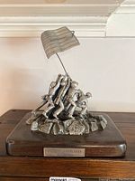Front and side view photo of the Iwo Jima statue showing six soldiers raising the American flag on a rocky base with a wooden platform and front plaque.