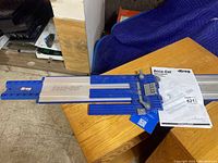 Blue and gray aluminum guide rail system with clamps and measurement markings on a wooden surface, alongside owner's manual.