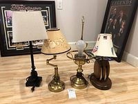 Set of four table lamps with varied styles and bases, including metal, brass, and wood; different lamp shades or missing shade on one.