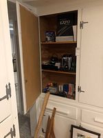 Cabinet with three shelves holding various office and school supplies including yardsticks leaning against the cabinet frame.