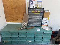 Full view of large teal metal organizer cabinet with many labeled drawers and miscellaneous items on top.
