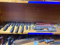 Top shelf showing several pipe wrenches with plastic grips, metal adjustable wrenches, and clamps