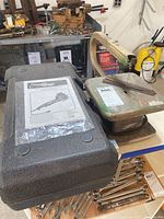 Heavy-duty green metal scroll saw on bench with blades and tools nearby.