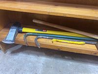 Photo of axe, two pry bars, and maul on wooden shelf.