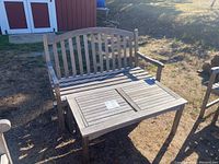 Outdoor wooden rocking bench with slatted back and armrests next to matching table.