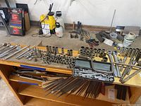 Wide view of assorted sockets and ratchets laid out on a wooden shelf/work surface with some additional hand tools and containers in the background