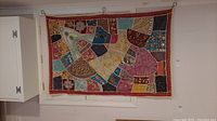Full view of the colorful patchwork fabric tapestry hanging on wall, showing overall size and composition.