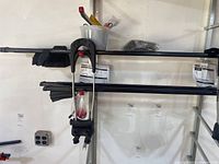 Two black Thule crossbars mounted on wall rack with TK1 installation kits attached, visible straps and mounting hardware bundled at the ends. Thule 430 Tracker II rack arms included, hanging on wall.