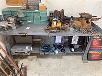 Full view of metal workbench surface with various tools and clamps arranged on top and underneath.