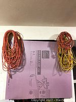 Photo of six coiled extension cords in orange, yellow, and red colors hanging on a wall.