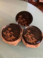 Top view of three stacks of black lacquer plates with gold tree and bird scenic designs on top.