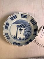Photo showing close-up detail of one bowl's design with man and birdcage in blue on white ceramic, scalloped edges with geometric patterns.