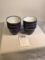Two stacks of four blue and gold porcelain teacups on white cloth, showing exterior and interior view.