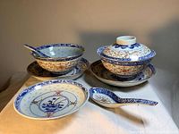 Overall view of two plates, two rice bowls with lids, and two spoons on cloth background