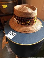 Woven straw pork pie hat on top of the Brooks Brothers hat box, showing patterned band and general shape.