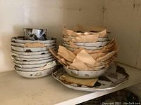 Dishes stacked with paper between them to protect surfaces. Shows different sizes including a cup on top of one stack.