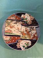 Top view of Chinese Export Imari charger plate showing detailed colorful floral and bird scene in multiple panels, rich cobalt blue, rust red, green and gold colors.