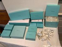 Photo showing multiple Tiffany & Co. boxes of different sizes arranged on table, open with visible empty interiors and white ribbons beside boxes.