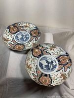 Two matching Imari porcelain plates resting on fabric, showing full front surface with Pagoda and Foo dog design.
