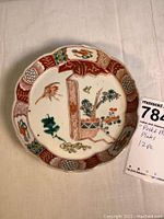 Single Imari-style decorative plate showing potted plant, bird, and floral motifs around scalloped edges.
