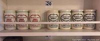 Seven cream-colored vintage glass jam jars, three labeled J. Keiler & Son Ltd. Ginger Preserve and four labeled Dundee Orange Marmalade, arranged on a shelf.