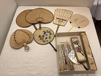 Overall collection of various Japanese hand fans laid out on a white surface.