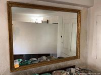 Front view of the large rectangular wall mirror with gold frame hanging on wall reflecting room interior including dishes and wall paneling.