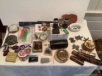 Photo showing the overall spread of miscellaneous assorted small items including lighters, candleholders, cartoon character dispensers, knife, binoculars, metal figurines, cigar tubes, pins, and other collectibles.