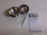 Two-piece set including silver tea strainer and stand displayed side by side.