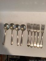Nine pieces of flatware: 5 forks and 4 soup spoons laid out on a white surface, showing shape and size.