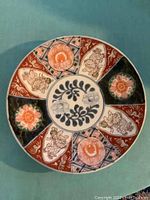 Top view of round Imari charger plate showing intricate floral and Shishi motifs in orange, green, and blue.