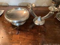 Two-piece set on wooden surface, one round pewter bowl and one two-arm candle holder in pewter.