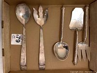Five silver plated serving utensils in cardboard box showing front view.