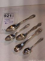 Top view of all five sterling spoons together on white surface showing size and design differences