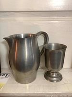 Front view of the wooden shelf with the pewter pitcher and mug displayed side-by-side.