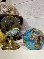 Clock and globe on display; clock has an inscription and nautical scene behind clock hands, globe shows continents in blue, brown, green, and other colors with grid lines.