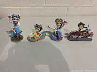 Four Betty Boop collectible figurines arranged on table, various themed poses including chopper sculpture and different shoes
