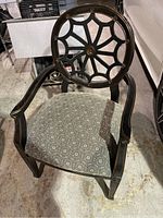 Front view of black and gold decorative chair showing carved circular backrest and patterned cushioned seat.