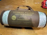 Pillow in brown nylon carrying bag with bamboo leaf fabric visible. Carrying bag printed with benefits and features of the memory foam bamboo pillow.