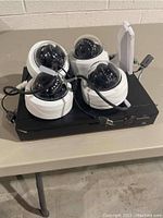 Four white dome cameras placed on top of a black DVR unit on a beige table.