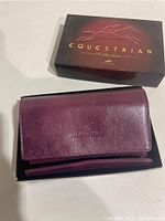 Burgundy wallet partially inside black box showing embossed Mancini logo on the front flap