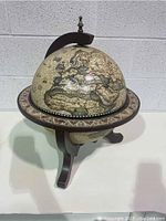 Antique style wooden globe closed, showing detailed map and dark wood stand with decorative paint on base.
