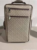 Front view of rolling carry on suitcase showing illustrated Guess 'G' logo pattern, exterior zippered pockets, top handle with faux crocodile texture.